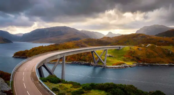 Un puente moderno cruza un fiordo escocés, con colinas otoñales y cielos dramáticos. La ruta 500 escocia ofrece vistas espectaculares.