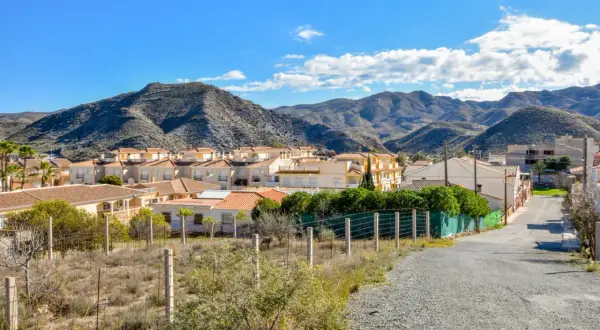 Casas blancas y tejados naranjas bajo montañas áridas en Los Lobos, Almería. Un camino de grava serpentea hacia el pueblo.