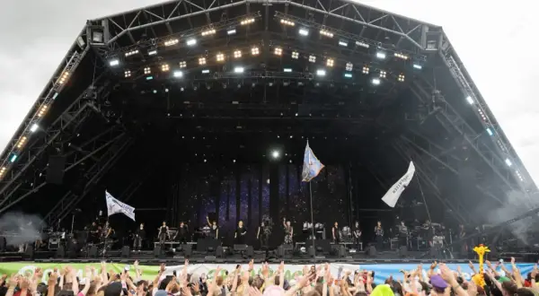 A massive crowd cheers at Glastonbury Festival, a testament to its huge capacity. Performers are on stage under a starry backdrop.