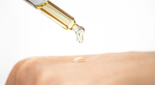 Tropfen eines goldenen Öls fallen aus einer Pipette auf die Haut. Glycerin ist ein Feuchtigkeitsspender, der die Haut geschmeidig macht.