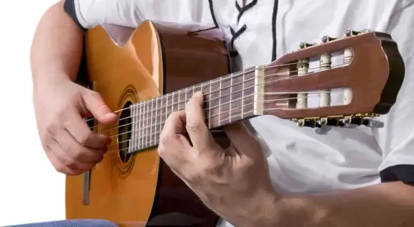 Dłonie grające na gitarze klasycznej, tworząc akordy po swojemu.
