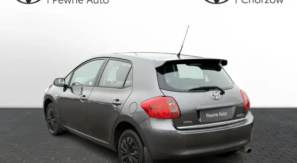 Szary Toyota Auris 2006 z przyciemnianymi szybami i spojlerem, zaparkowany na kostce brukowej.