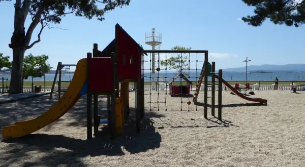 Un colorido parque infantil en la playa invita a jugar. Toboganes, redes y columpios esperan bajo el sol, con el mar de fondo.
