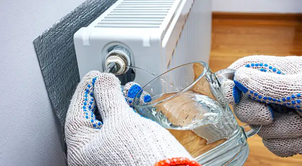 Mani guantate raccolgono acqua da un bicchiere mentre si impara come sfiatare i termosifoni, liberando l'aria intrappolata.