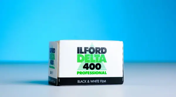 A box of Ilford Delta 400 Professional black and white film sits on a white surface against a bright blue background.