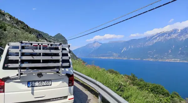 Biały bus z bagażnikiem rowerowym na tle jeziora i gór we Włoszech. Zastanawiasz się, ile trwa podróż do Włoch autokarem?