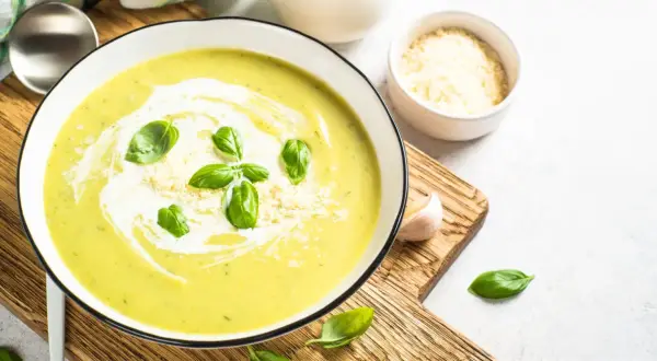 Aksamitna zupa krem z cukinii z warzywami, udekorowana listkami bazylii i parmezanem. Idealna na lekki obiad.