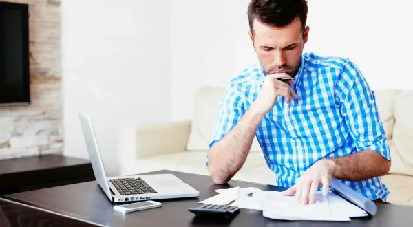 Mężczyzna w kratę analizuje dokumenty, obok laptop, telefon i kalkulator. Może to być jego ufg historia oc.