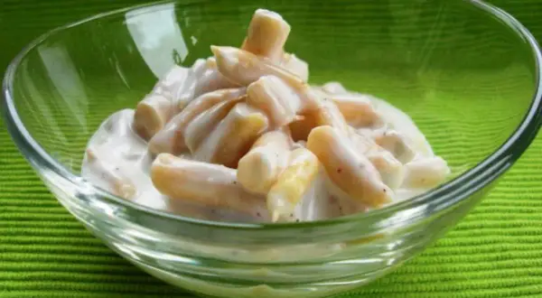 Gelber Bohnensalat in einer Glasschüssel auf grünem Hintergrund.