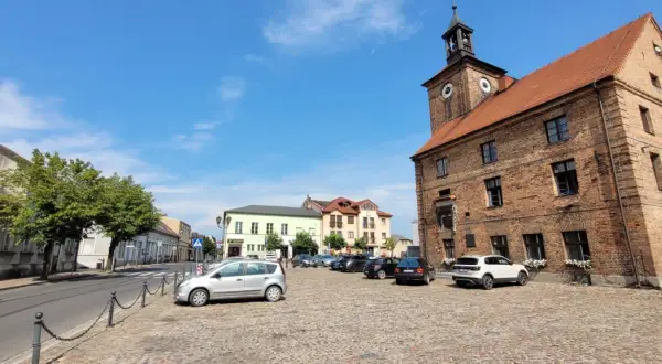 Rynek w Połajewie z zabytkowym ratuszem i kolorowymi kamienicami. Na brukowanym placu zaparkowane samochody.
