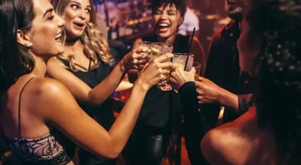 Glada vänner skålar i drinkar, en riktig Zakynthos fest-stämning på en livlig bar.