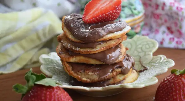 En hög med amerikanska pannkakor med nutella och färska jordgubbar. Pudrad med florsocker.