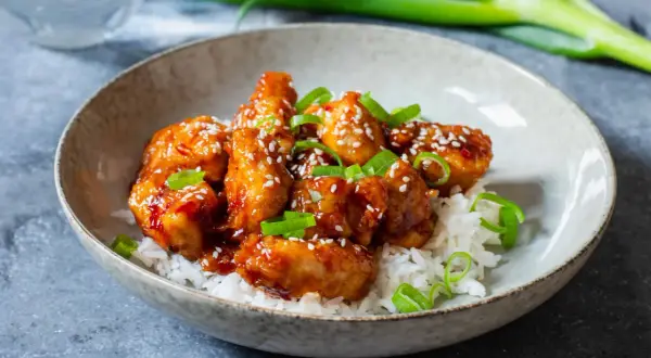 Krispiga kycklingbitar i en söt och syrlig sås, toppade med sesamfrön och salladslök. Ett perfekt recept med kyckling för en snabb middag.