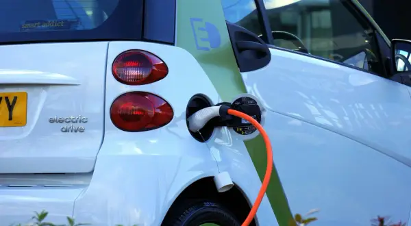 Voiture électrique blanche en charge, avec un câble orange branché. Le symbole "E" vert sur le flanc indique son caractère écologique. Le frais réel d'une voiture électrique est sa recharge.