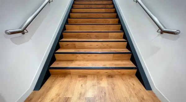 Moderne Treppe mit Holzoptik-Belag. Die Betonstufen sind professionell verkleidet, mit schwarzer Kante und Edelstahl-Handlauf.