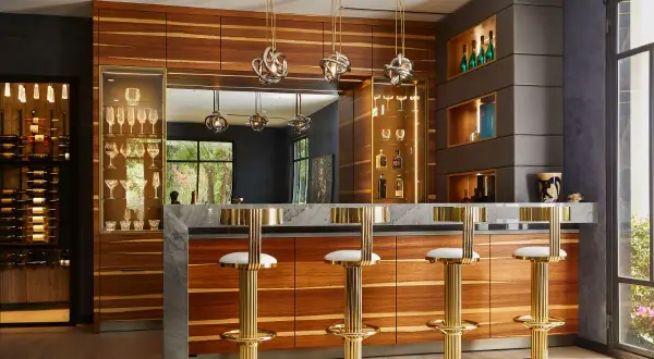 Luxurious home bar ideas featuring a marble countertop, wood cabinetry, gold bar stools, and a wine display.