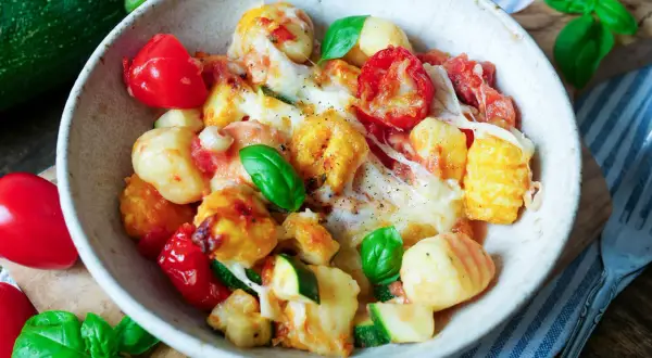 Herzhaftes Gnocchi Auflauf Rezept mit Tomaten, Zucchini und geschmolzenem Käse, garniert mit frischem Basilikum.