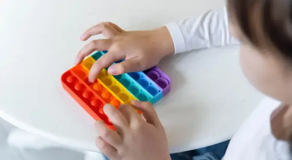 Dziecko bawi się tęczową zabawką sensoryczną typu pop it.