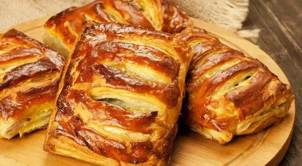 Złociste, pieczone ciasto francuskie z nadzieniem, ułożone na drewnianej desce.