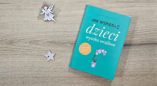 Książka "Jak wspierać dzieci wysoko wrażliwe" na drewnianym tle, obok aniołka i gwiazdki.