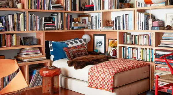 Gemütliches Lesezimmer einrichten mit Bücherregalen voller Bücher, einem Bett, einem Ledersessel und einem roten Stuhl.