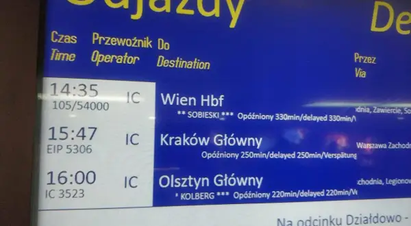 Tablica odjazdów pociągów pokazuje, jak sprawdzić opóźnienie pociągu. Widać opóźnione pociągi do Wiednia, Krakowa i Olsztyna.