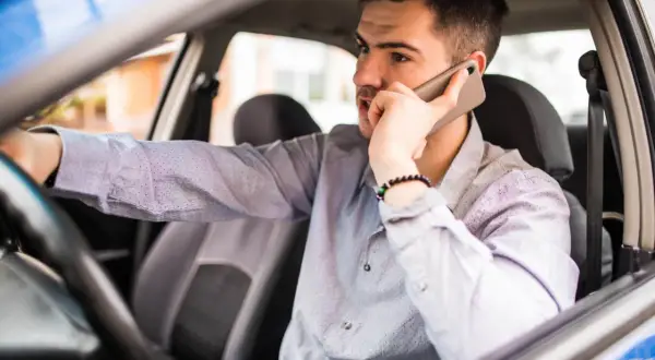Mężczyzna za kierownicą rozmawia przez telefon, martwiąc się o mandaty w Szwajcarii.