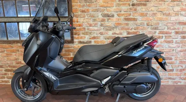 Czarny skuter Yamaha X-Max 125 na tle ceglanej ściany i okna.
