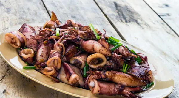Assiette d'encornets sautés, une délicieuse recette encornet, garnie de ciboule fraîche sur une table en bois.