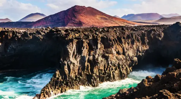 Wulkaniczne klify na Lanzarote, turkusowe morze i góry w oddali. Idealna pogoda na odkrywanie tej wyspy.