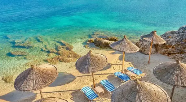 Piękna plaża w Albanii z turkusową wodą i słomianymi parasolami. Zastanawiasz się, ile się leci do Albanii?