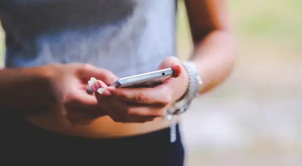 Dłonie z zadbanymi paznokciami trzymają srebrny telefon. To zrzut ekranu Samsunga, uchwycony w letnim otoczeniu.