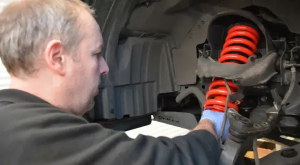 Mechanik w niebieskiej rękawiczce pracuje nad nowym, czerwonym, wylany amortyzator.