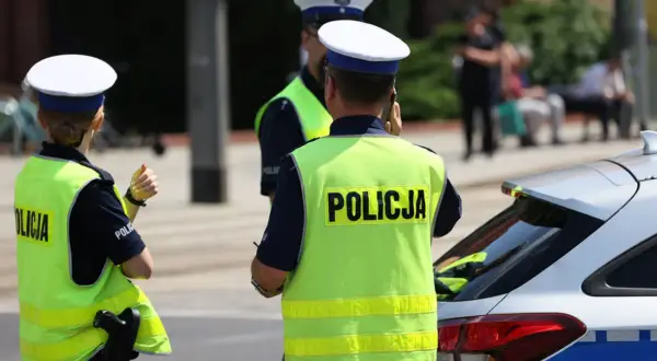 Policjanci w kamizelkach odblaskowych stoją obok radiowozu. Czy policja może wejść na teren prywatny bez nakazu?
