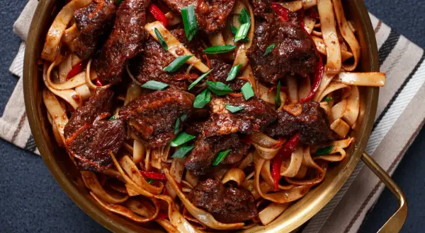 Wołowina po syczuańsku z makaronem, papryczkami chili i szczypiorkiem w złotej misie.