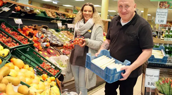 Mann und Frau im Markt Refrath mit frischem Obst und Gemüse. Er hält eine Kiste Spargel, sie Erdbeeren.