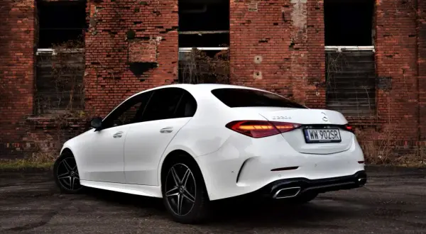 Biały Mercedes C 220 d z czarnymi felgami na tle zrujnowanej ceglanej ściany.