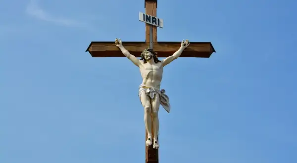 Figurka Jezusa na drewnianym krzyżu z tabliczką INRI na tle błękitnego nieba.