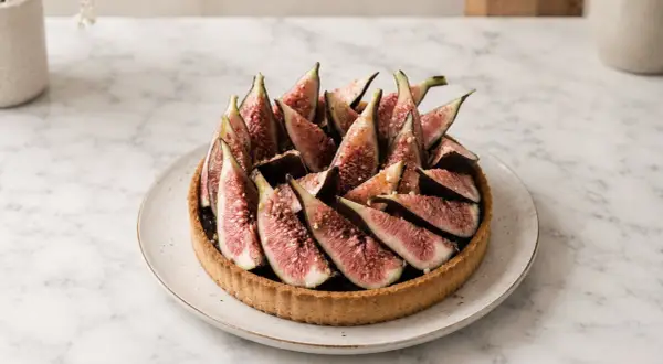 Tarte aux figues fraîchement préparée, garnie de quartiers de figues rouges et d'une touche de noix concassées. Un délice visuel et gustatif.