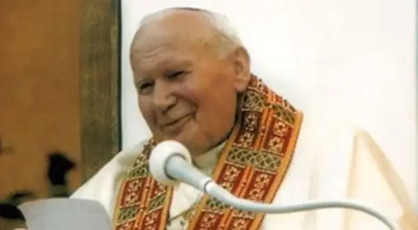 Jan Paweł II z uśmiechem przemawia do wiernych, trzymając w ręku tekst. Jego barki zdobi ozdobna stuła.