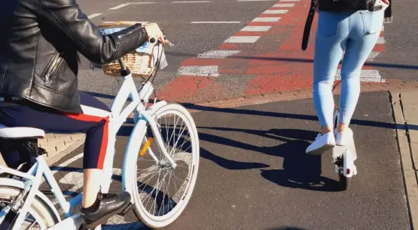 Osoba na rowerze i osoba na hulajnodze elektrycznej jadą po ścieżce rowerowej.