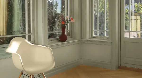 En ljus hall med en vit stol och en vas med blommor på fönsterbrädan. Väggarna är målade i en lugn grön nyans, vilket ger en harmonisk känsla.