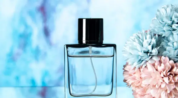 Elegancka butelka perfum lataffa z czarną nakrętką, obok pastelowych kwiatów.