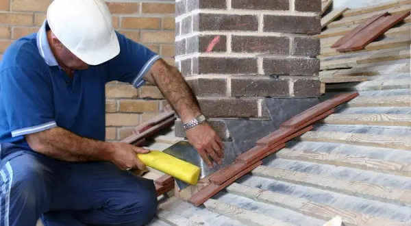 Un couvreur assure l'étanchéité de la cheminée sur la toiture avec du plomb et des tuiles.