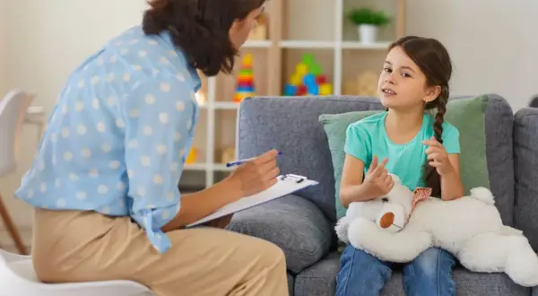 Dziewczynka z misiem rozmawia z psychologiem, który notuje na kartce.