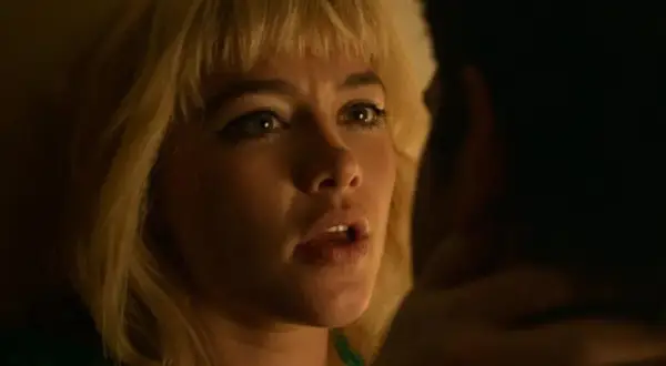 Zbliżenie na Florence Pugh w jednym z jej filmów. Jej blond włosy i wyraziste oczy przyciągają uwagę.