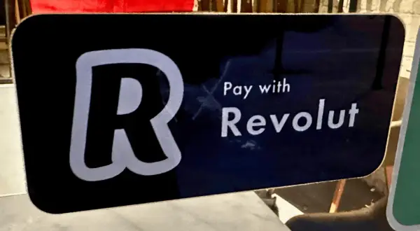 Znak informuje, jak płacić Revolutem. Widoczny duży symbol "R" i napis "Pay with Revolut".