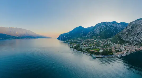 Panoramica del Lago di Garda con montagne imponenti e una città pittoresca. Perfetto per scoprire le **Unternehmungen Gardasee**.