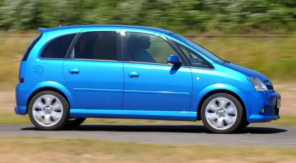 Błękitny Opel Meriva 1.4 benzyna w ruchu, z widocznym kierowcą za przyciemnianą szybą.