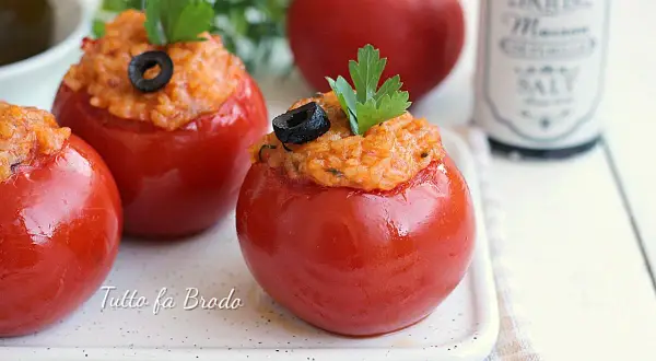 Pomodori ripieni di riso, guarniti con olive nere e prezzemolo, su un piatto bianco.